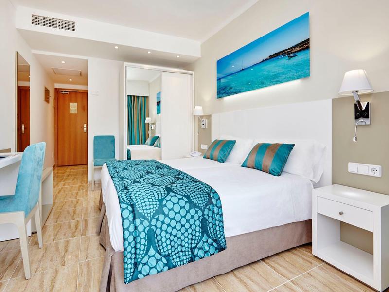 Nowoczesny pokój hotelowy z łóżkiem podwójnym, niebieską narzutą i drewnianą podłogą.