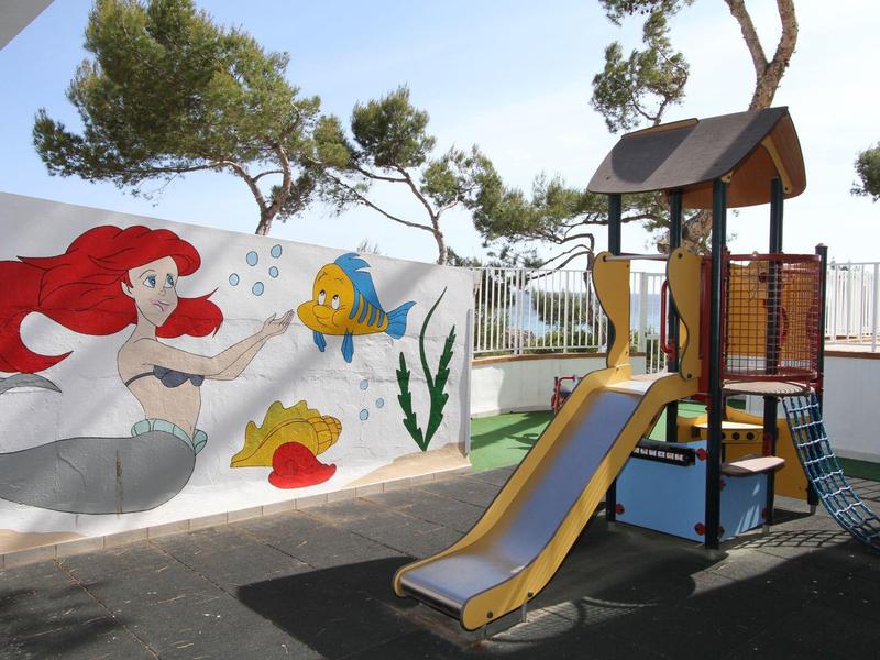 Plac zabaw dla dzieci ze zjeżdżalnią przed ścianą z kolorowymi morskimi malunkami.