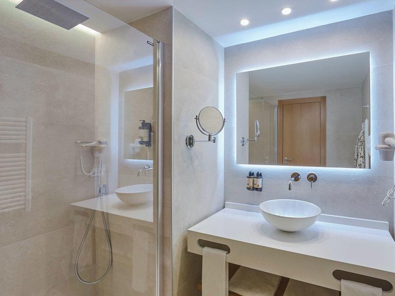 Nowoczesna łazienka hotelowa z podświetlanym lustrem, wolnostojącą umywalką i osobnym prysznicem.