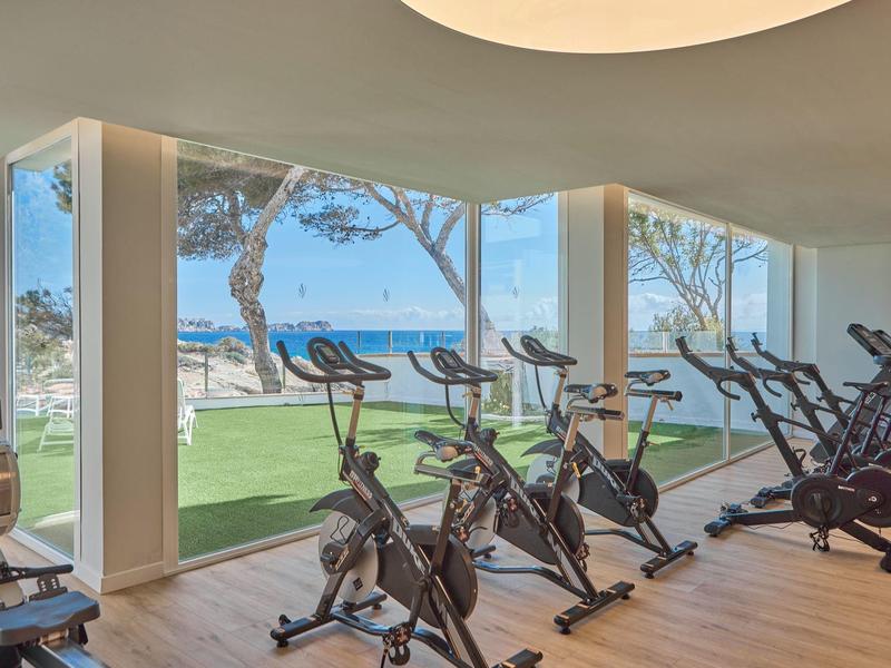 Siłownia z rowerami stacjonarnymi i widokiem na plażę oraz morze przez duże okna.