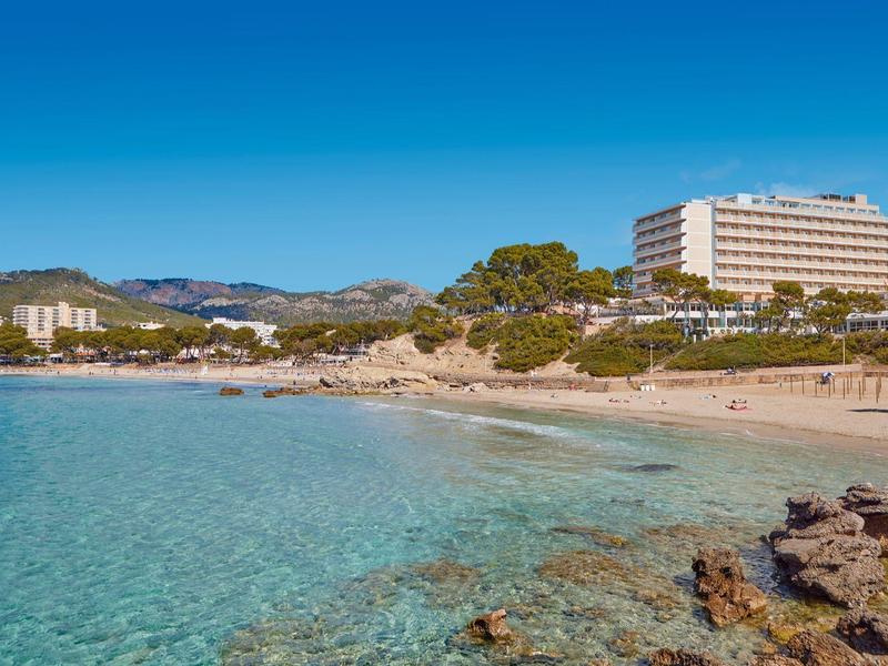 Przejrzyste niebieskie morze z skałami i budynkami hotelowymi na słonecznej plaży.