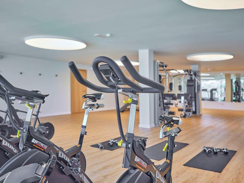 Nowoczesna siłownia z rowerami stacjonarnymi, ciężarkami i dużymi lustrami.