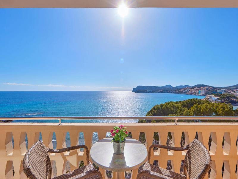 Balkon z stołem, krzesłami i kwiatami z widokiem na morze i słoneczne wybrzeże.