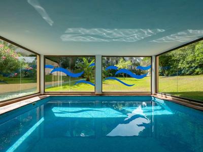 Innenraum eines Schwimmbads mit klarem Wasser, großen Fenstern und bunten Delfin-Motiven an der Decke.