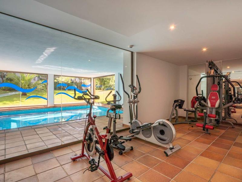 Heimtrainer und Crosstrainer in modernem Fitnessraum neben Schwimmbad mit großer Glaswand.