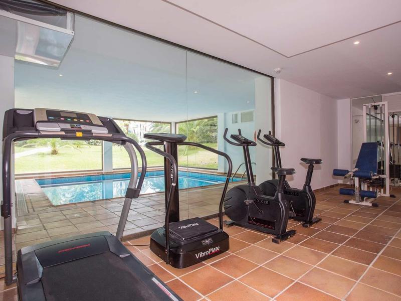 Fitnessraum mit Laufband, Ergometern, Kraftmaschine und großem Fenster zum Außenpool.