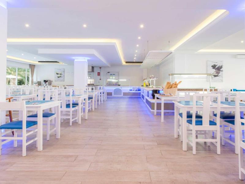 Helles, modern eingerichtetes Restaurant mit weißen Möbeln und blauen Sitzpolstern, Holzboden.