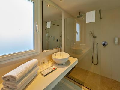 Bagno moderno con lavabo, finestra, asciugamani e doccia a filo.