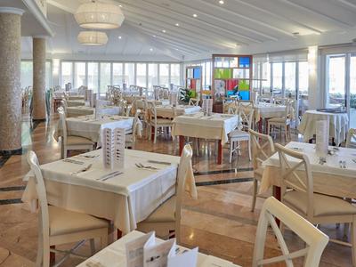 Ristorante luminoso e spazioso con tavoli e sedie bianchi e grandi finestre con vista sul mare.