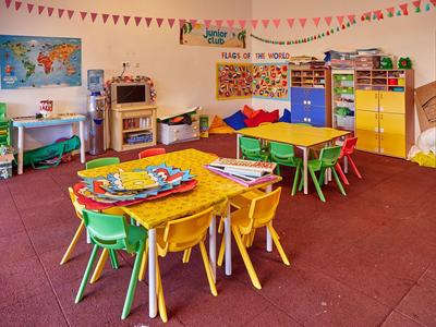 Aula di asilo colorata con piccoli tavoli, sedie e materiali didattici ludici.