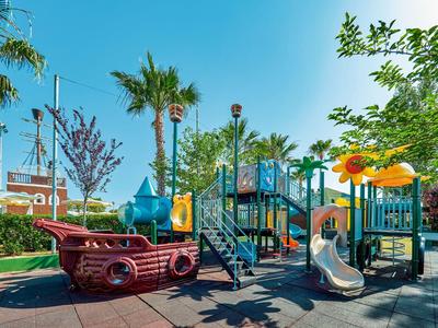 Colorato parco giochi per bambini con scivoli e nave pirata sotto il sole.