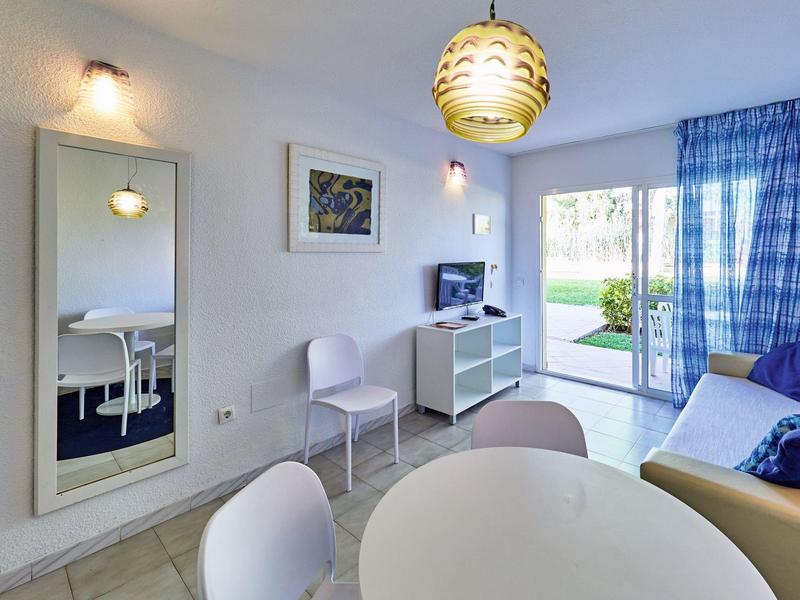 Soggiorno luminoso con zona pranzo, mobili bianchi e vista su un giardino attraverso una porta scorrevole in vetro.