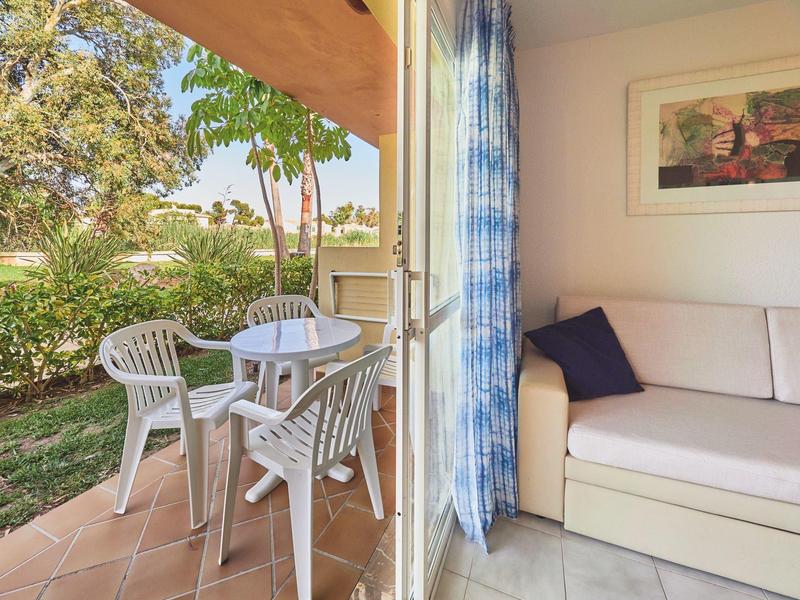 Vista da un soggiorno con divano su una terrazza con tavolo da giardino bianco e sedie.