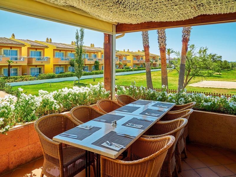 Terrazza coperta con tavolo apparecchiato, vista su aree verdi e edifici gialli.