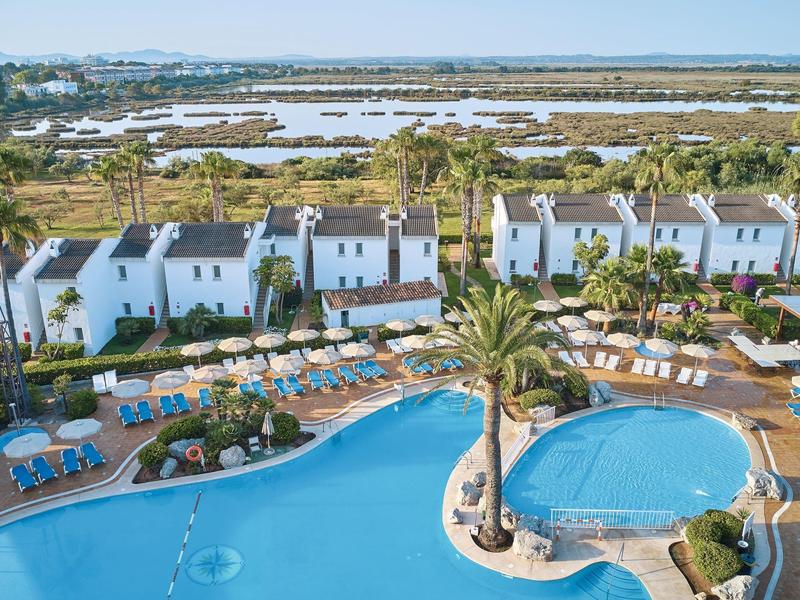 Hotel con due piscine, palme e edifici bianchi vicino a zone umide.