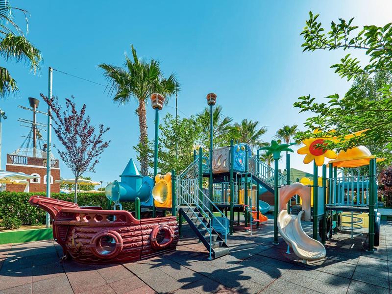 Colorato parco giochi per bambini con scivoli e nave pirata sotto il sole.