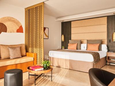 Modernes Hotelzimmer mit Doppelbett, Sitzecke, Holzboden und warmen Farben.