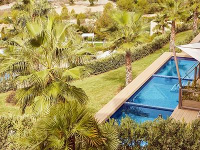 Hotelgarten mit Pool, Palmen und grüner Landschaft in sonniger Umgebung