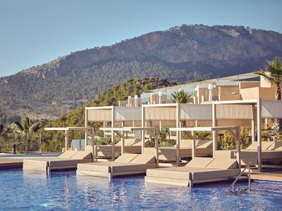 Luxe zwembad met ligstoelen en modern hotelgebouw tegen een berglandschap onder een heldere hemel