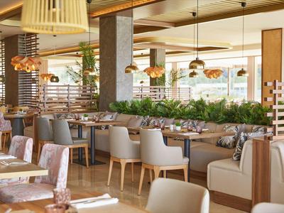 Modern gestaltetes Restaurant mit beigen Stühlen und hängenden Lampen im Tageslicht.