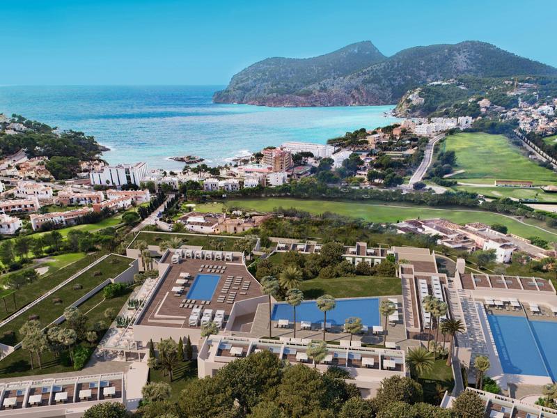 Luftaufnahme eines Resorts mit Pools, Beachvolleyballfeld und Küstenblick bei klarem Himmel.