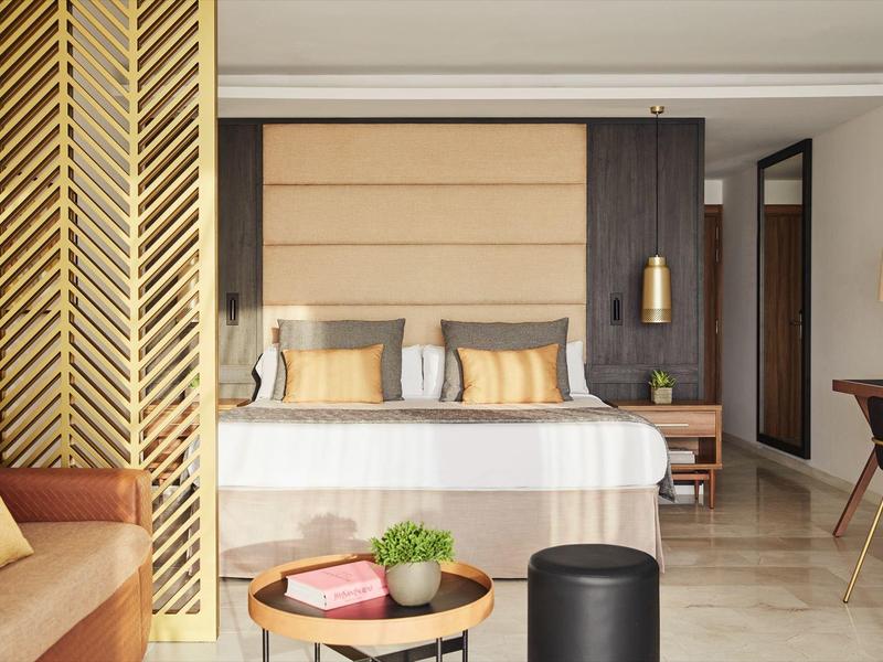 Modernes Hotelzimmer mit großem Bett, goldenen Akzenten und Sitzbereich mit Sofa und Tisch.