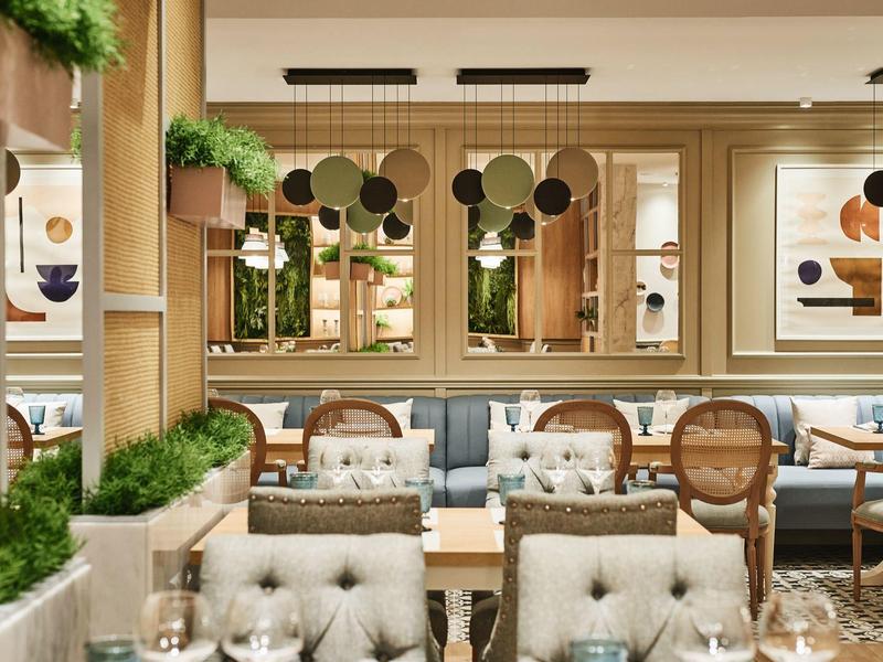 Helles Restaurantinterieur mit hölzernen Möbeln, grünen Pflanzen und abstrakter Kunst an den Wänden