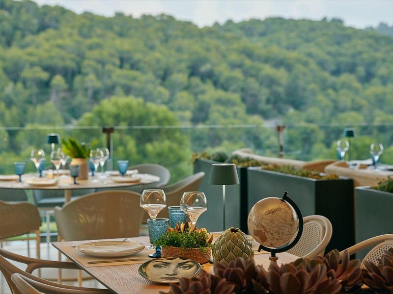Terrasse mit eingedeckten Tischen und Blick auf bewaldete Hügel im Hintergrund.