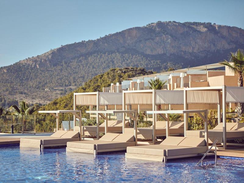 Moderner Hotelpool mit Liegen vor Bergkulisse bei klarem Himmel