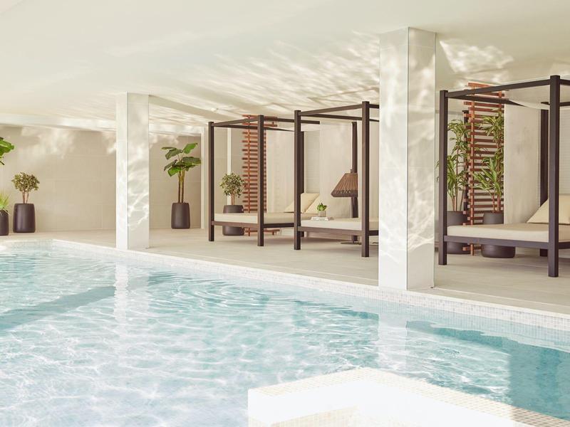 Innenpool mit flachen Liegen und Pflanzen in einem modernen Spa-Bereich.