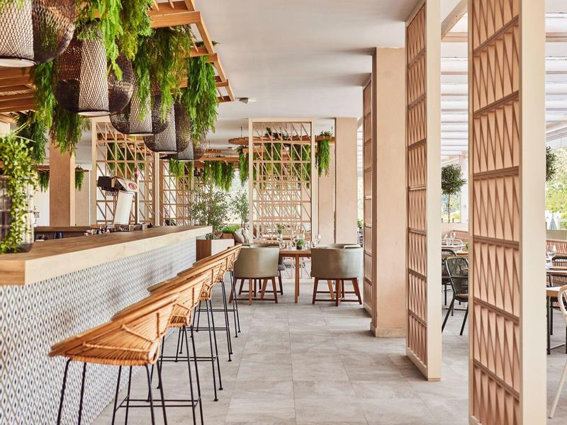 Elegante Hotelbar mit Holzstühlen, Pflanzen und modernem Design.