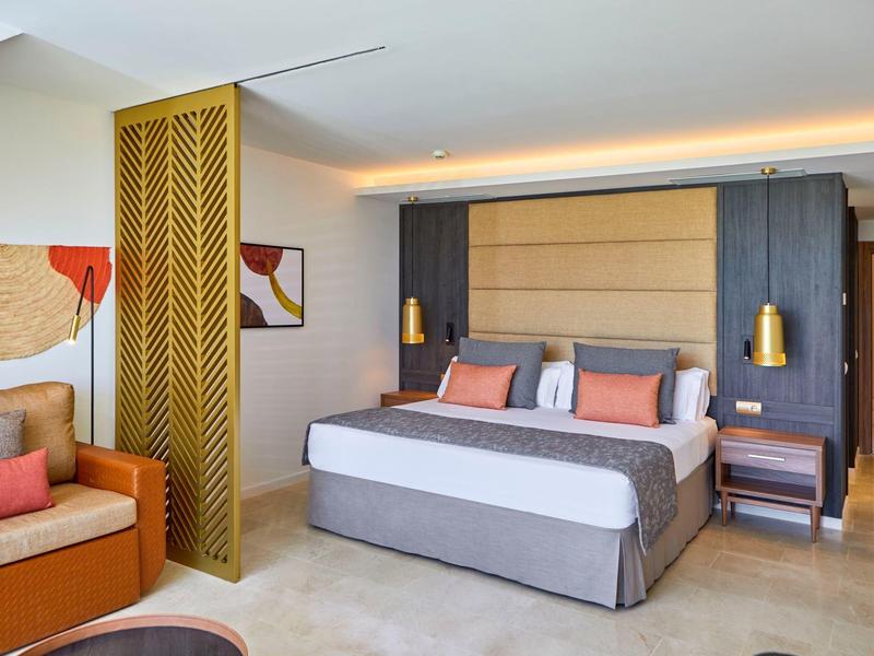 Modern eingerichtetes Hotelzimmer mit großem Bett, gemütlichem Sofa und dekorativer Trennwand.