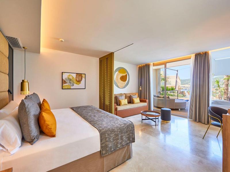 Modern eingerichtetes Hotelzimmer mit großem Bett und Balkon mit Sitzbereich.