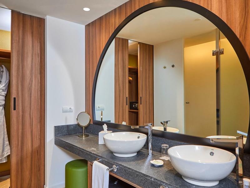 Modernes Badezimmer mit rundem Spiegel, zwei weißen Waschbecken und Holzmöbeln