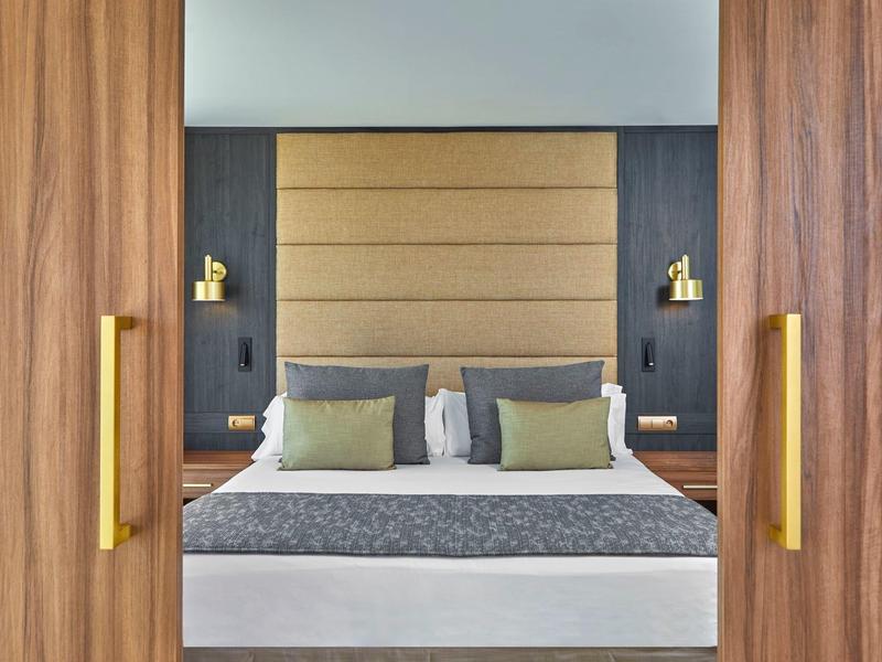 Modernes Hotelzimmer mit Doppelbett, grauen Kissen und verstellbaren Leselampen.