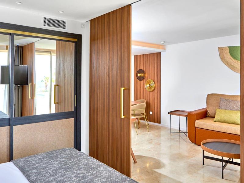 Modernes Hotelzimmer mit Holzakzenten, großem Spiegel, Schreibtisch und gemütlichem Sitzbereich.