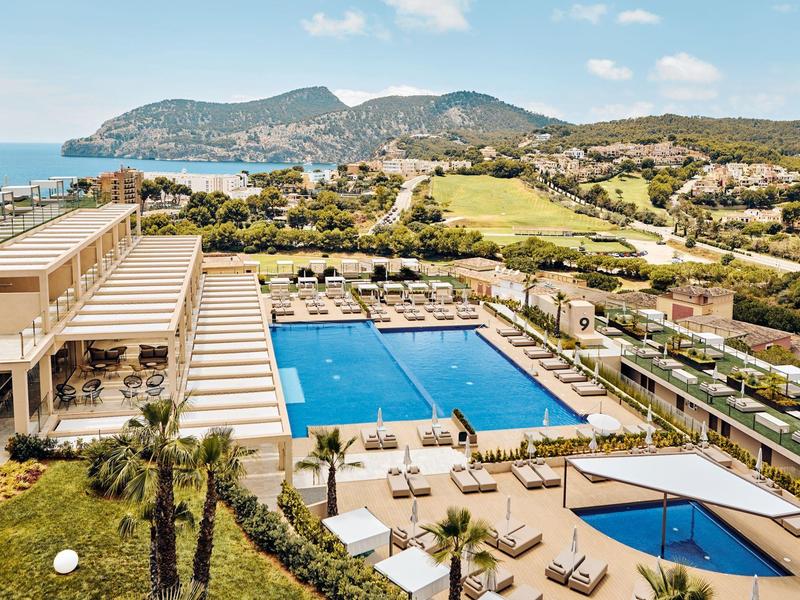 Großer Außenpool mit Liegestühlen und Blick auf Hügel und Meer an einem sonnigen Tag.