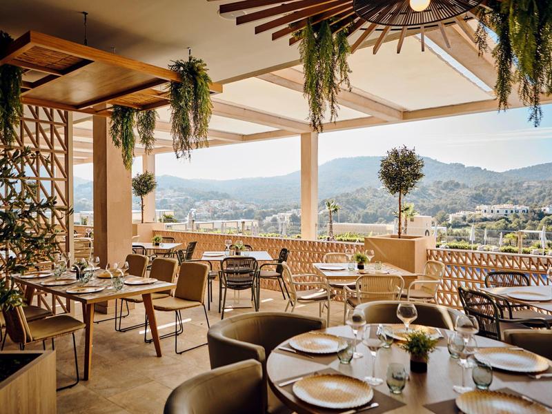 Offenes Restaurant mit Blick auf Berge und Stadt, mit gedeckten Tischen und Pflanzen.