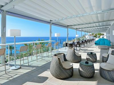 Terraza abierta del hotel con muebles modernos y vista al mar azul bajo un cielo despejado.