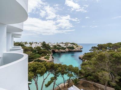 Vista desde un balcón blanco hacia una bahía con agua clara y árboles verdes bajo un cielo nublado.