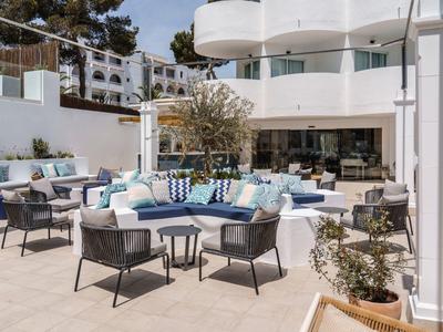 Buitenterras van hotel met moderne stoelen, ronde banken en kussens rond tafels in fel licht.
