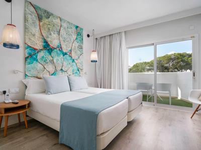 Habitación de hotel moderna con dos camas, grandes ventanales con vista a áreas verdes, decoración luminosa.