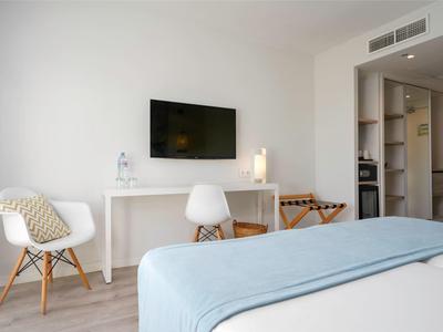 Habitación de hotel moderna con televisor, escritorio, sillas y una cama con manta azul clara.