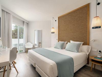 Habitación de hotel moderna con cama doble, ventana grande y decoración elegante en tonos neutros.