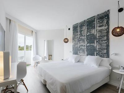 Habitación de hotel moderna con cama doble, ventana grande y decoración elegante en tonos neutros.