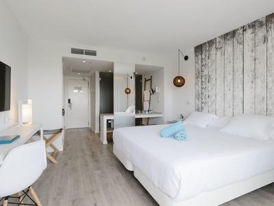 Habitación de hotel luminosa con cama doble, suelo de madera y decoración moderna.