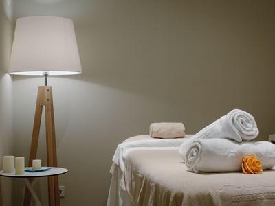 Área de bienestar acogedora con camilla, toallas blancas y luz cálida de lámpara de pie.