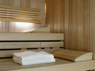 Sauna de madera clara con toallas blancas dobladas y reposacabezas sobre el banco.
