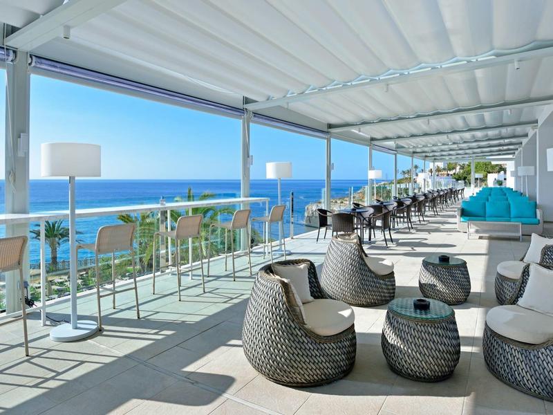 Terraza abierta del hotel con muebles modernos y vista al mar azul bajo un cielo despejado.
