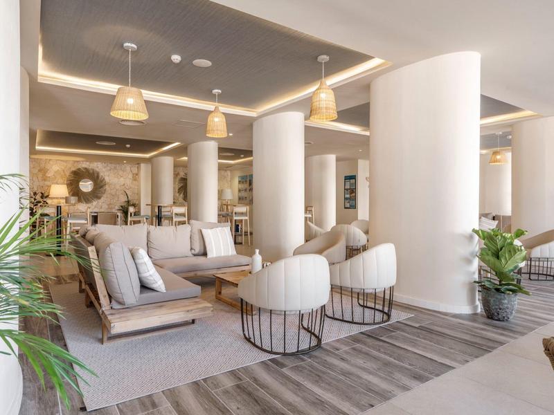 Área de salón de hotel moderno con sillones cómodos, sofás y iluminación elegante.